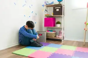 Child sitting on foam mat in a therapy or playroom setting.
