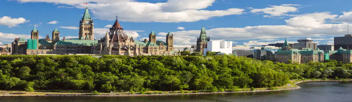 Ottawa skyline featuring Parliament Hill and green riverbank.