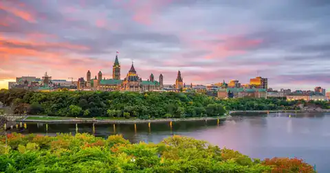 Ottawa skyline featuring Parliament Hill and green riverbank.